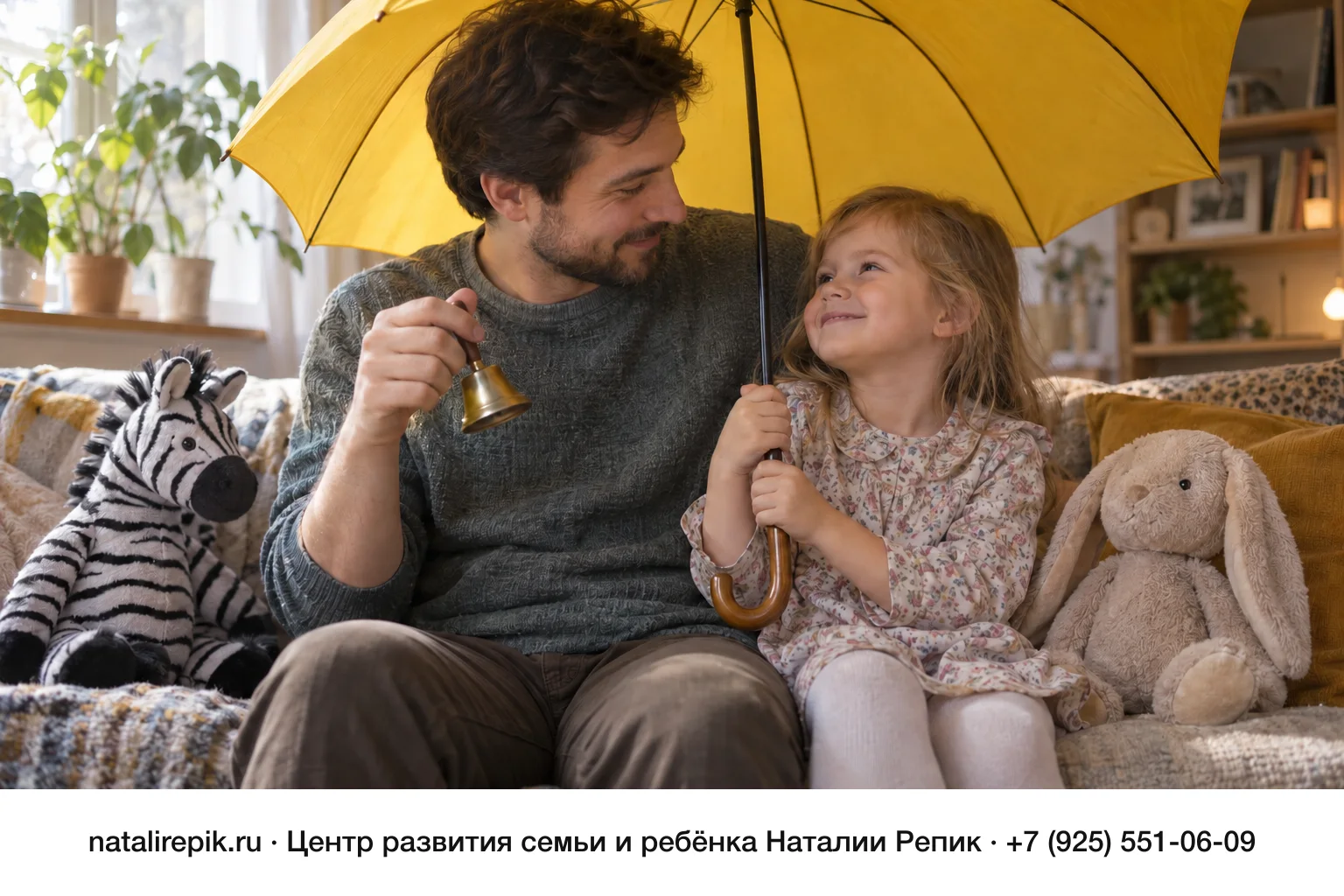 Папа и четырёхлетняя дочка сидят на диване под раскрытым жёлтым зонтом, как под навесом; папа держит маленький колокольчик, рядом плюшевая зебра и зайка, девочка смеётся