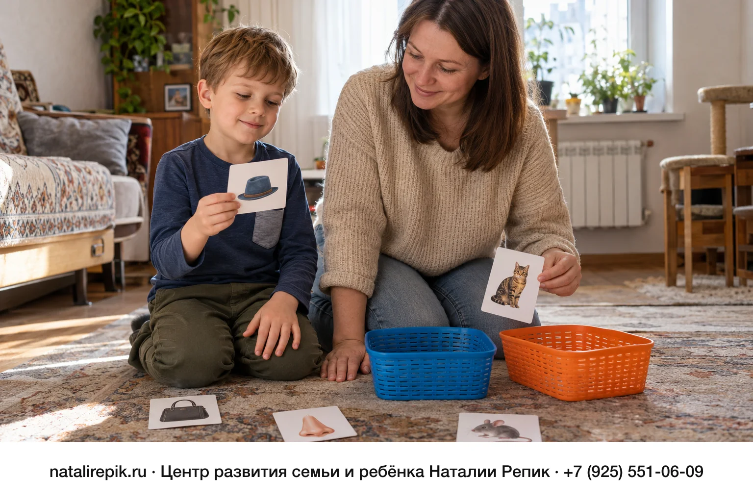 Мама и шестилетний сын сидят на ковре и сортируют картинки-карточки с обычными предметами по двум корзинкам, синей и оранжевой; мальчик держит карточку со шляпой, мама — карточку с кошкой