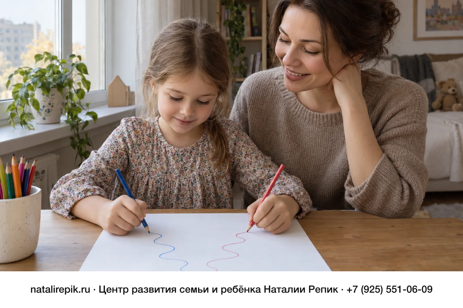 Мама и шестилетняя девочка сидят за столом у окна: девочка держит по карандашу в каждой руке и одновременно рисует две волнистые линии на одном листе, синюю и красную, мама наблюдает с улыбкой