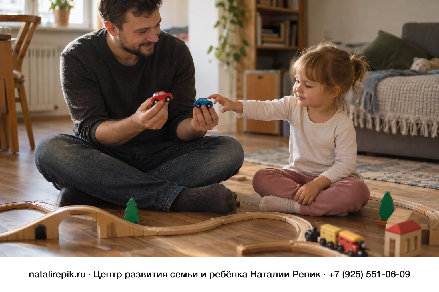 Папа сидит по-турецки на деревянном полу с двумя игрушечными машинками в руках и предлагает их двухлетней девочке, девочка тянется к одной из них, вокруг собрана деревянная железная дорога
