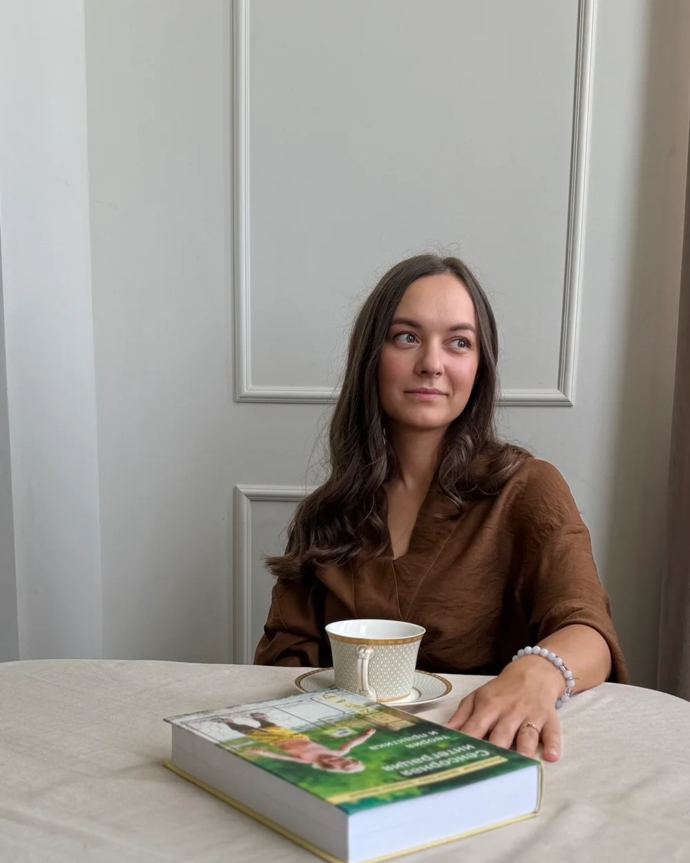 Наталия Репик за столом с книгой и чашкой, настоящая фотография из домашней фотосессии