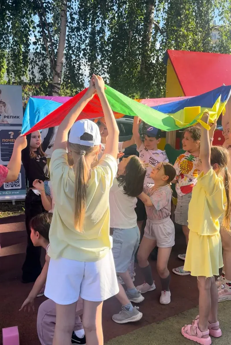 Дети играют с радужным парашютом