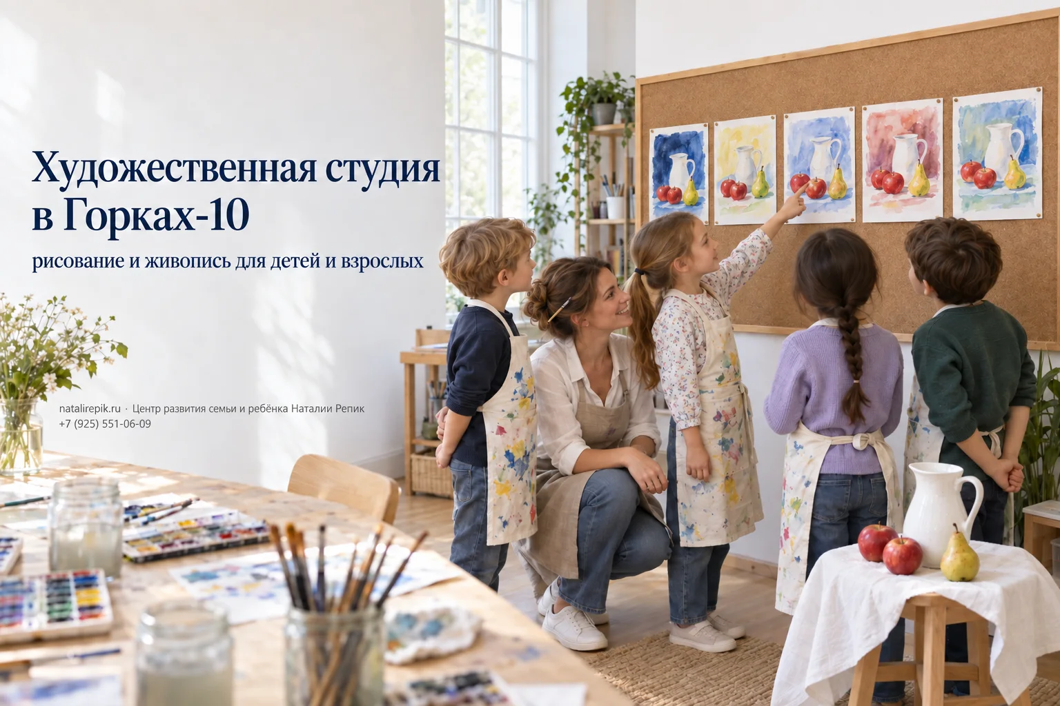 Дети в фартуках вместе с педагогом рассматривают свои акварели с одним натюрмортом — кувшин, яблоки и груша; девочка показывает на свою работу