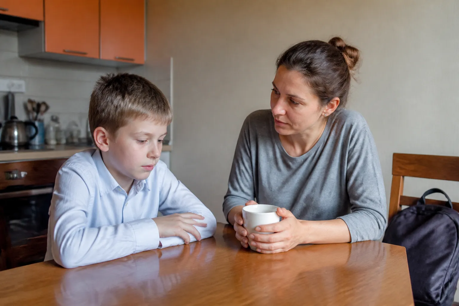 Встревоженный школьник утром за кухонным столом, мама сидит рядом и слушает его